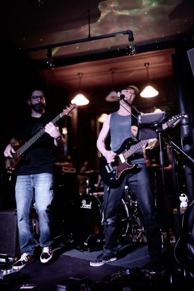 Live-Band im Sir Capulus in Füssen: Zwei Musiker mit E-Gitarre und Bass spielen auf der Bühne, Konzertatmosphäre in der Bar im Allgäu. 